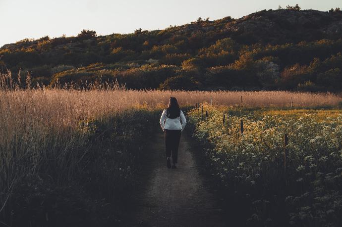 woman walks between flowers and wheat during daytime